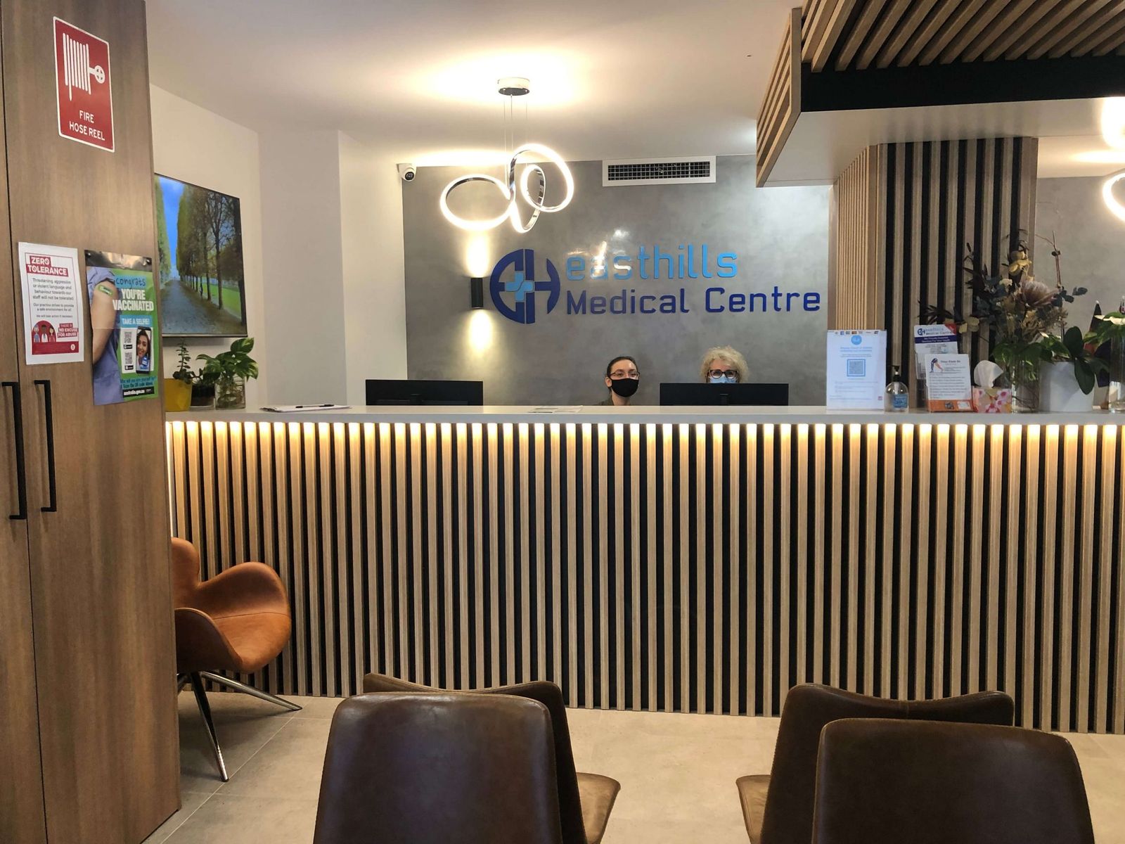 Front desk of East Hills Medical Centre with two reception staff and timber slat counter