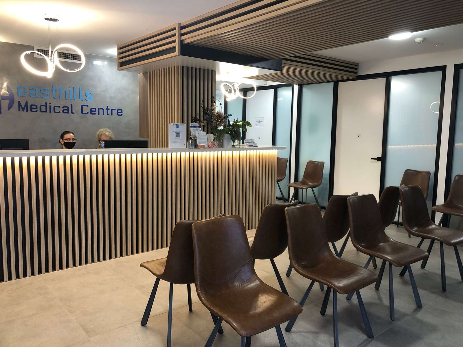 Reception desk at East Hills Medical Centre with oak timber slats and the practice logo on the wall